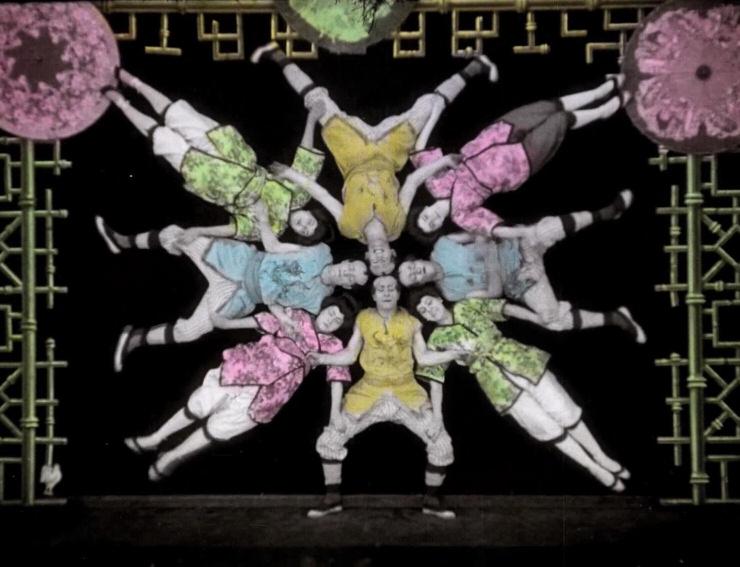 In the first number four women and four men appear, forming a star-shaped human pyramid sending coloured rays out in front of the black backdrop.
