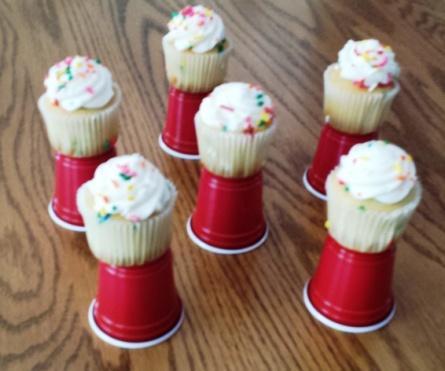 Purchase some very small plastic red drink cups and have someone bake mini-cupcakes with yellow cupcake papers and dark icing on top. (White icing is pictured.