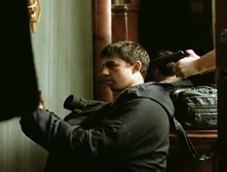 Through the open door frame, the camera frames Danila and a hand belonging to somebody off-screen holding a gun to his back (figure 1.3. a-b).