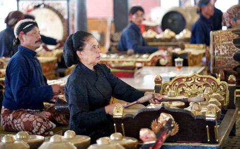 Woman in traditional garb playing gong during a performance by traditional gamelan