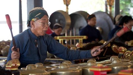 Man in traditional garb playing gong during a performance by traditional gamelan