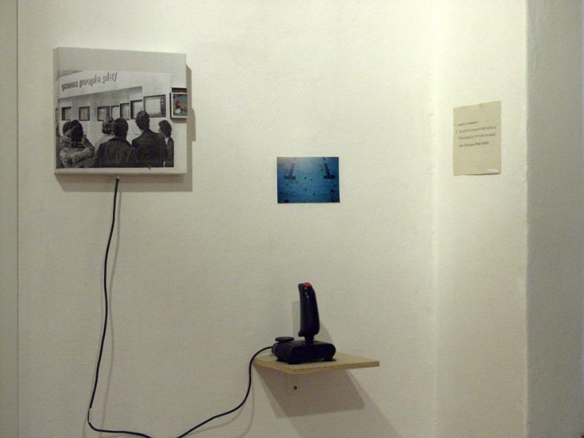 SLIKA 20: Sašo Vrabič, Igre, ki se jih ljudje igrajo, 2003, računalniški tisk (25 cm x 27 cm), lepenka, igralna palica, zvočni modul, interaktivni objekt To je ena izmed postavitev, ki je bila na že