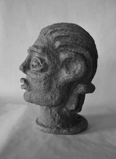 (Foto: Tereza in Štěpán Axman) SLIKA 12: Pokončna fotografija prikazuje glineno skulpturo človeške glave z neizrazitim obrazom, slikano v levi profil.