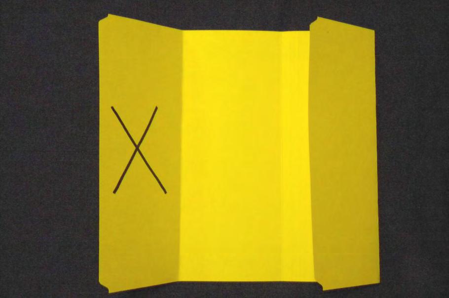 Apply glue or double-sided tape to this X flap. With the X flap lying open, pick up the other file folder (in these photos, the green folder), holding it so its flaps are closed.