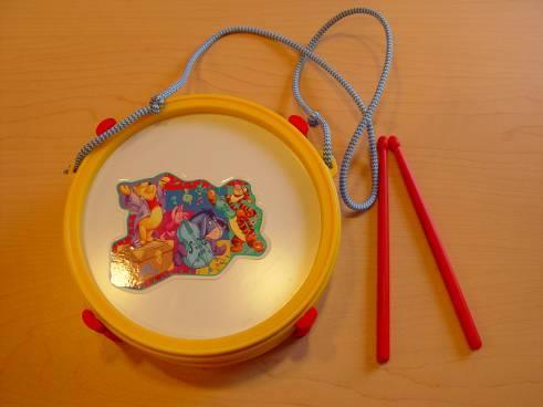 Small plastic drum with 2 sticks and cord to hang around the neck. Brightly coloured, with well-known cartoon figures on the membrane intended for hitting.